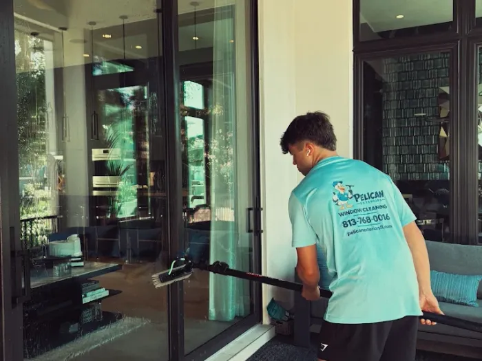 Pelican Exteriors technician in branded uniform cleaning lanai sliding doors in Tampa