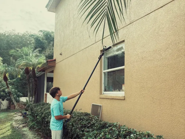 Technician cleaning a window above a hedge at a Tampa home